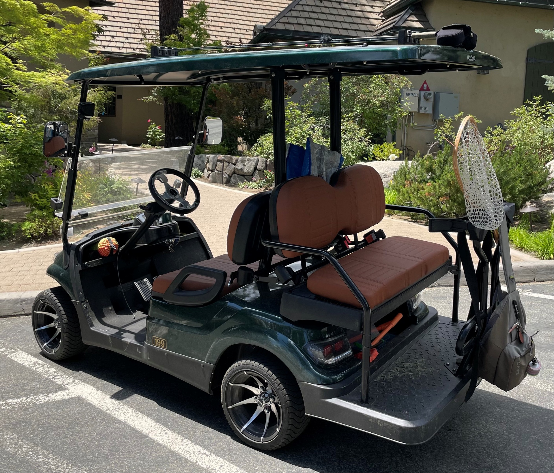 Montreux member golf cart outfitted with a fly-fishing net and rod, parked along a paver drive at the clubhouse