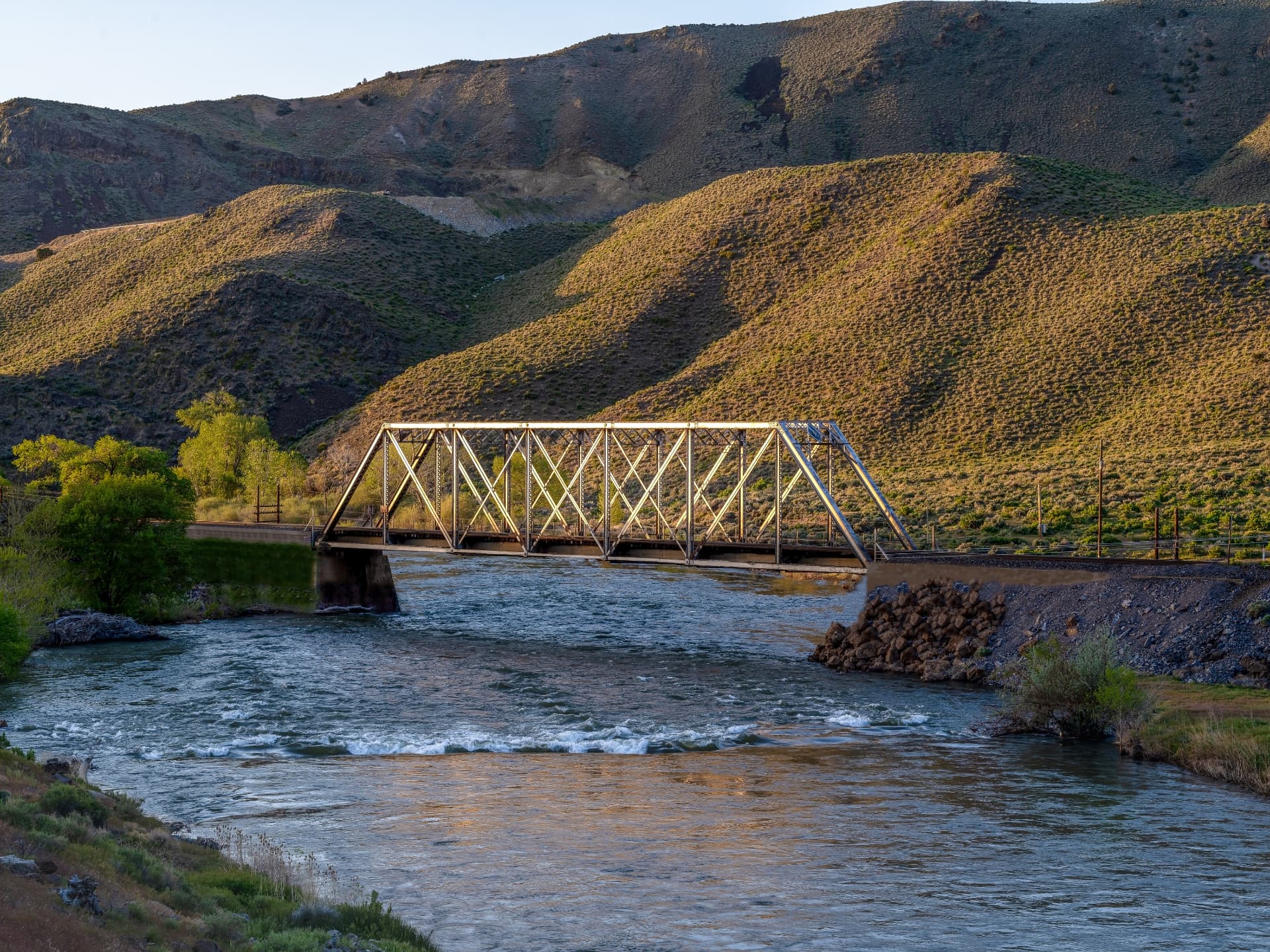 Historic steel truss railroad bridge spanning the Truckee River at golden hour below sagebrush hills